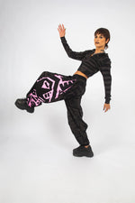 Model leaning against wall in charcoal and pink BAM‑BAM poppa pants and bra top, artistic streetwear