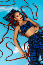 Model lying on blue background in BAM‑BAM dark blue bra top and trousers reflecting self‑expression