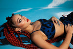 Close up of model lying on blue background in BAM‑BAM dark blue bra top and trousers reflecting self‑expression
