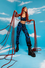 Model holding her red hair on blue background in BAM‑BAM dark blue bra top and trousers reflecting self‑expression