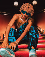 Male model posing on red stairs in BAM‑BAM dark blue dungarees, showcasing wearable art and sustainable streetwear